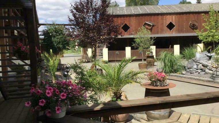 Ein wunderschöner Innenhof mit Pflanzen und bunten Blumen. Im Hintergrund sind Gebäude aus Holz und eine kleine Wasseranlage zu sehen.