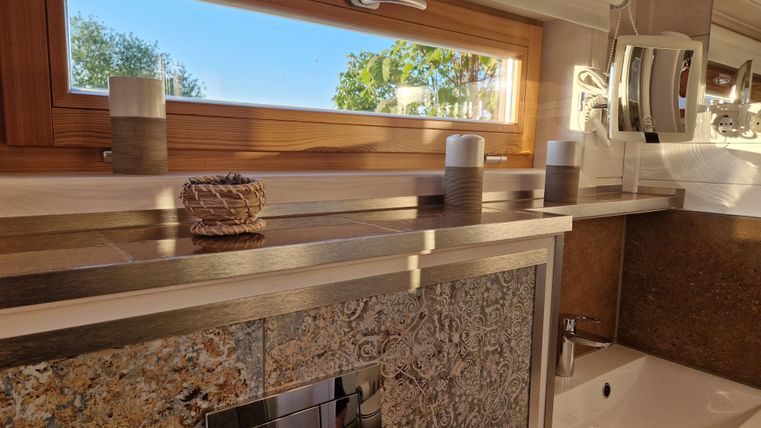 Ein modernes Badezimmer mit einem Fenster, das Tageslicht hereingelassen. Auf dem Tisch stehen Kerzen und ein dekoratives Element.