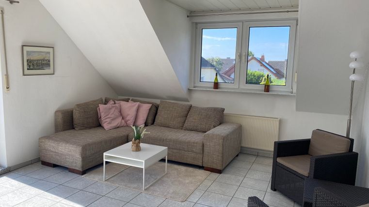 Ein helles Wohnzimmer mit einer gemütlichen Couch und einem kleinen Tisch. Große Fenster sorgen für viel Tageslicht.