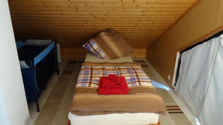 Ein gemütliches Dachzimmer mit einem Einzelbett und einem Kissen. Ein rotes Handtuch liegt auf der Bettdecke.