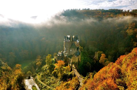 Burg Eltz im herbstlichen Licht, umgeben von Wald. 
