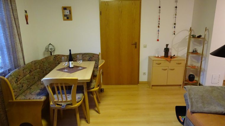 Ein gemütlicher Wohnbereich mit einem Esstisch und Stühlen. An der Wand hängen Dekorationen, und eine Tür führt in einen anderen Raum.