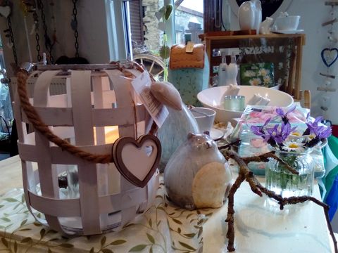 Eine hübsche Deko mit einem laternenartigen Korb und einer kleinen Figur. Im Hintergrund sind verschiedene Geschirr- und Dekorationsgegenstände zu sehen.