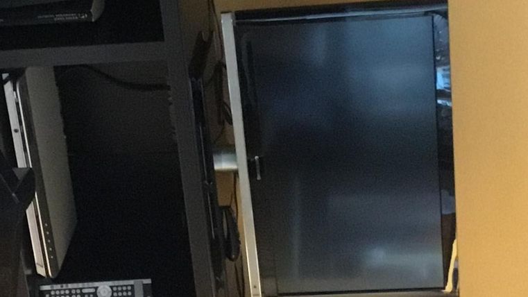 Ein modernes Wohnzimmer mit einem Fernseher und Lautsprechern. Auf einem Regal stehen Bücher und eine gläserne Vase.