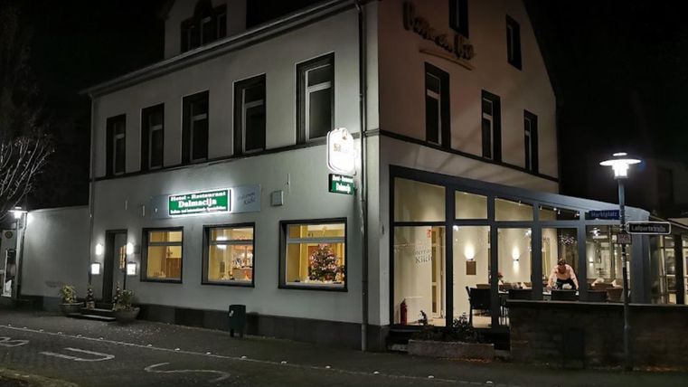 Ein Restaurantgebäude bei Nacht, beleuchtet von warmem Licht. Die Fenster zeigen eine einladende Atmosphäre mit Gästen drinnen.