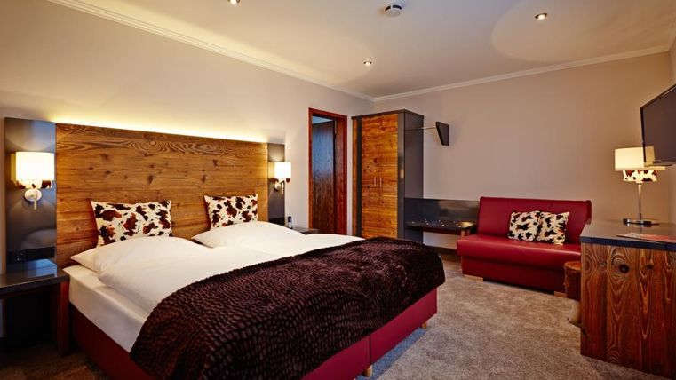 Ein modernes Schlafzimmer mit einem Doppelbett und gemütlichen Kissen. Es gibt eine rote Couch und Holzdetails, die dem Raum eine warme Atmosphäre verleihen.