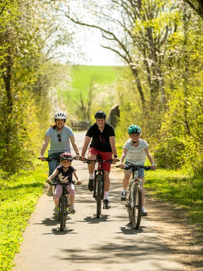 Kinder und Eltern auf Fahrrädern radeln auf dem Maifeld-Radweg.
