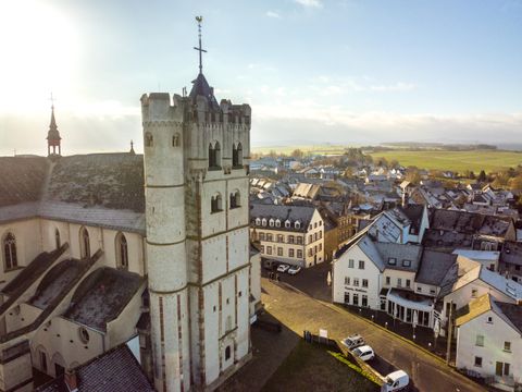 Une église historique avec un clocher marquant se trouve au milieu d'une petite ville. Les environs montrent une architecture typiquement allemande et un paysage vallonné en arrière-plan.