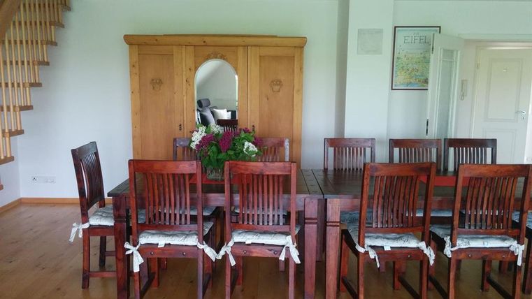 Ein stilvoller Essbereich mit einem großen Holztisch und Stühlen. Im Hintergrund steht ein Holzschrank mit einer schönen Blumenarrangement.