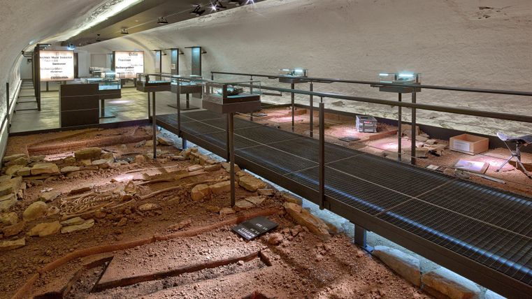 Ein archäologisches Museum mit Ausgrabungen und Informationen. Es gibt Stege und beleuchtete Exponate in einem historischen Raum.