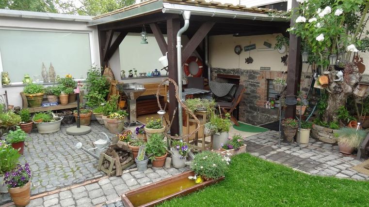 Ein gemütlicher Garten mit einer überdachten Sitzecke und vielen Pflanzen in Töpfen. Der Rasen ist grün und gepflegt, ideal für entspannte Stunden im Freien.