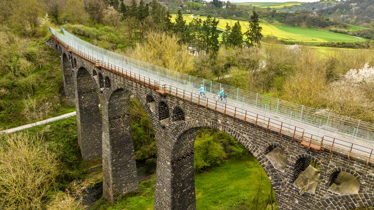 Zwei Radfahrer auf dem Nette-Viadukt des Maifeld-Radwanderwegs, umgeben von grüner Landschaft und Bäumen.