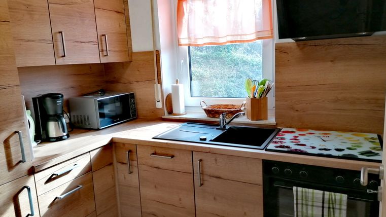 Eine moderne Küche mit Holzschränken und viel Tageslicht. Sie enthält Geräte wie einen Wasserkocher, eine Mikrowelle und einen Herd.