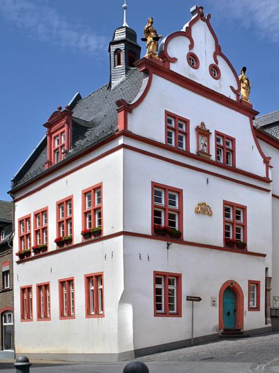 Ein historisches Gebäude mit einer weißen Fassade und roten Akzenten. Es hat viele Fenster und eine auffällige Dachstruktur.