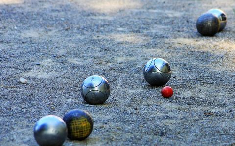 Eine Boule-Bahn mit mehreren Kugeln im Sand. Eine rote Kugel liegt in der Nähe der silbernen Kugeln.