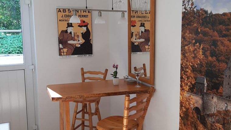 Un petit coin confortable avec une table en bois et deux chaises. Des affiches nostalgiques sont accrochées au mur et des boissons sont posées sur la table.