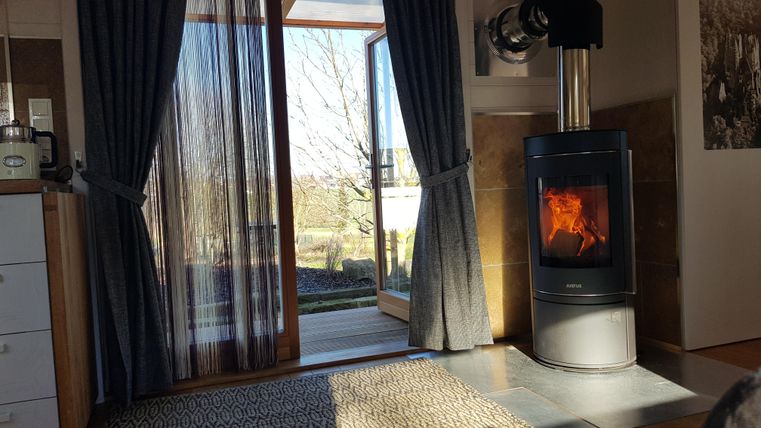 Ein gemütliches Wohnzimmer mit einem modernen Kamin und großen Fenstern. Das Licht strömt herein und sorgt für eine warme Atmosphäre.