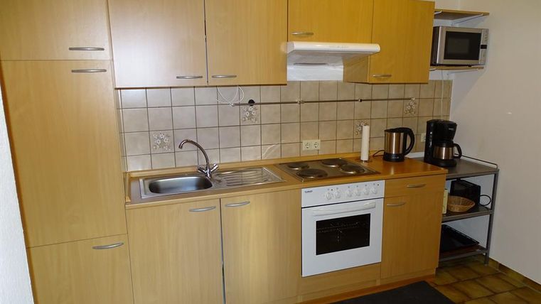 Eine moderne Küche mit Holzschränken, Herd und Spüle. Neben einem Kühlschrank steht eine Mikrowelle und eine Kaffeemaschine.