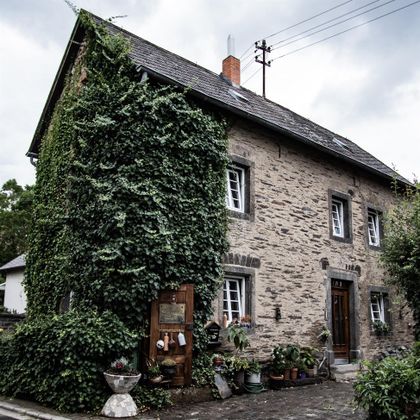 Ein charmantes, altes Steinhaus, das von üppigem Grün umgeben ist. Die Fassade zeigt eine Kombination aus Natur und traditioneller Architektur.