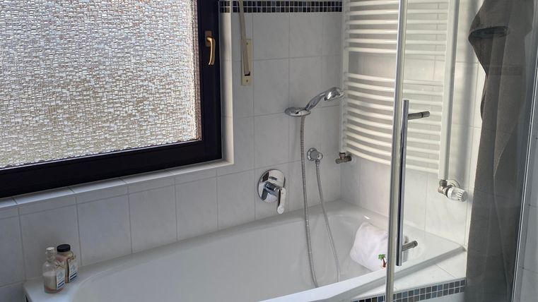 Ein modernes Badezimmer mit einer Badewanne und einer separaten Dusche. Große Fenster sorgen für viel Tageslicht.