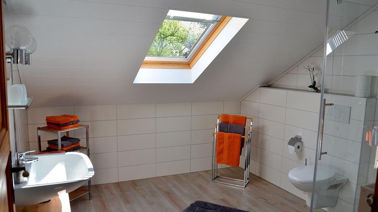 Ein modernes Badezimmer mit einer Dachfenster und warmen Farbtönen. Es gibt eine Dusche, ein Waschbecken und Handtücher in orange.