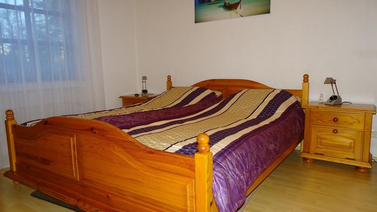 Ein gemütliches Schlafzimmer mit einem Holzbett und bunten Bettdecken. Neben dem Bett stehen zwei Nachtische und ein Fenster sorgt für Tageslicht.