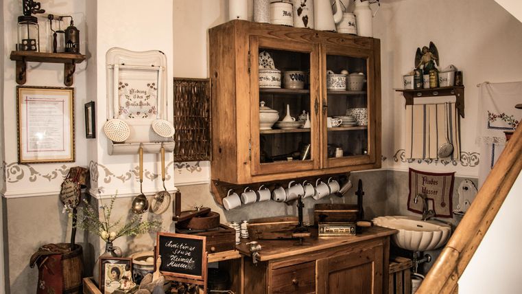 Eine gemütliche Küchenecke mit einem Holzschrank und verschiedenen Küchenutensilien. Die Wände sind dekorativ gestaltet und vermitteln ein rustikales Ambiente.