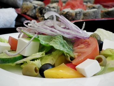 Ein frischer Salat mit verschiedenen Gemüsesorten wie Tomaten, Gurken und Zwiebeln. Ergänzt wird er durch Oliven und Feta-Käse.