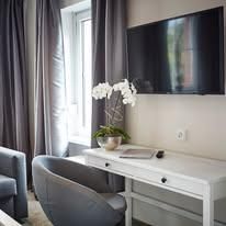 Ein modernes Zimmer mit einem Schreibtisch und einem Fernseher. Auf dem Tisch steht eine Orchideenpflanze und es gibt graue Vorhänge.