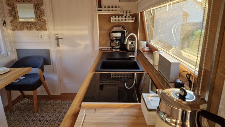 Eine moderne Küche mit Holzregalen und großen Fenstern. Auf der Theke stehen eine Kaffeemaschine und ein Wasserkocher.