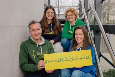 die vier Mitglieder des Tourismus-Teams Maifeld mit dem #maifeldschatz-Schild auf der Treppe sitzend