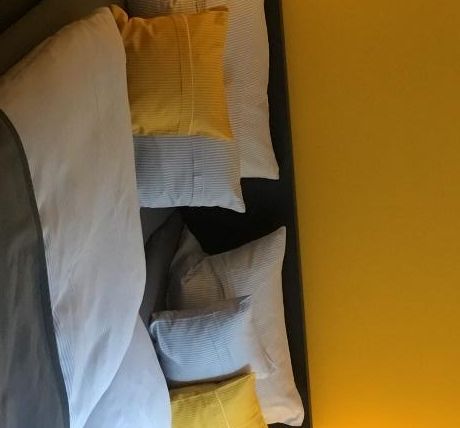 Ein gemütliches Schlafzimmer mit einem großen Bett und bunten Kissen. Die Wände sind in einem warmen Gelbton gehalten, und zwei Tischlampen sorgen für eine angenehme Beleuchtung.