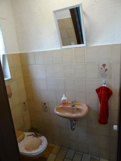 Ein kleines Badezimmer mit einem Waschbecken und einer Toilette. An der Wand hängt ein rotes Handtuch.