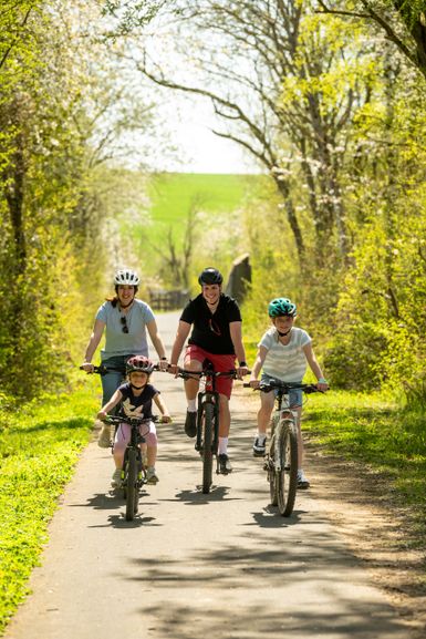Kinder und Eltern auf Fahrrädern radeln auf dem Maifeld-Radweg.