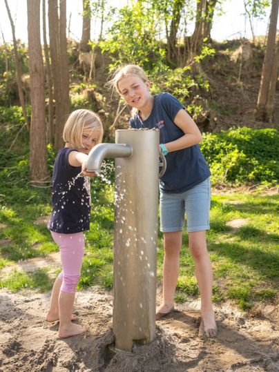 Zwei Mädchen pumpen Wasser auf dem Wasserpielplatz am Maifeld-Radweg