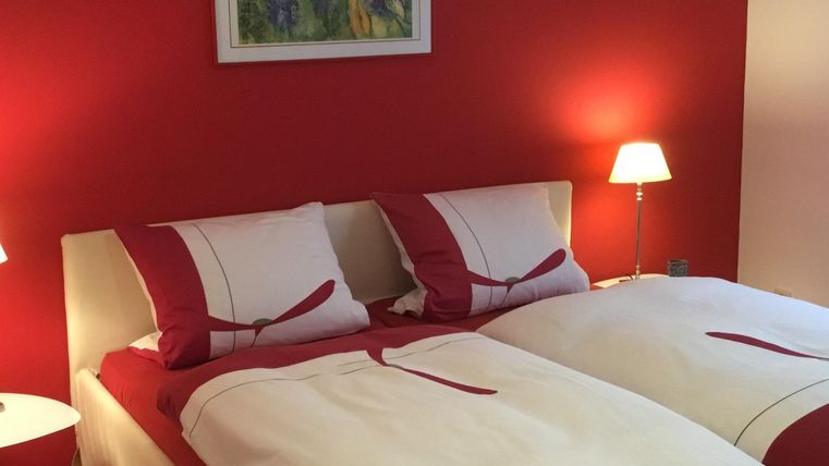 Ein gemütliches Schlafzimmer mit roten Wänden und zwei Einzelbetten. Die sanfte Beleuchtung sorgt für eine entspannte Atmosphäre.