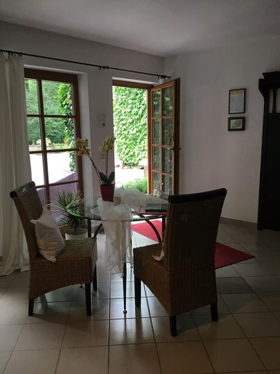 Ein heller Raum mit einem runden Glastisch und zwei Stühlen. Die offene Tür führt in einen grünen Gartenbereich.