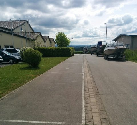 Eine ruhige Straße zwischen Wohngebäuden, mit parkenden Autos auf der linken Seite. Am Ende der Straße steht ein Boot auf einem Anhänger.