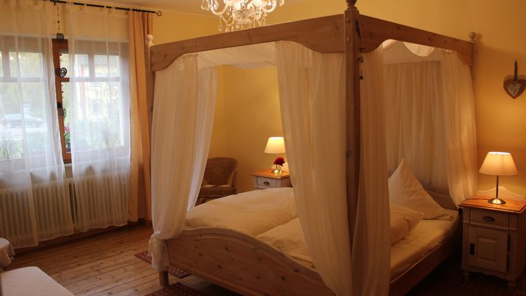 Ein gemütliches Schlafzimmer mit einem Himmelbett und warmen Farben. Weiche Beleuchtung sorgt für eine einladende Atmosphäre.