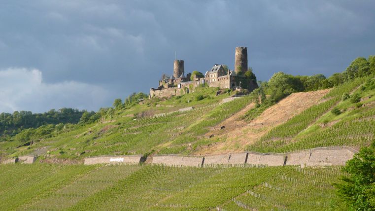 Eine alte Burgruine erhebt sich auf einem grünen Hügel. Dunkle, bewölkte Himmel sorgen für eine dramatische Atmosphäre.