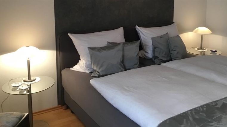 Ein modernes Schlafzimmer mit einem gemütlichen Bett und eleganten Kissen. Neben dem Bett steht ein Nachttisch mit einer Lampe.