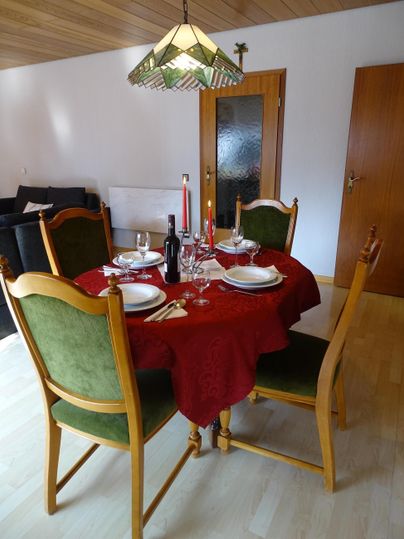 Een gedekte tafel met een rode doek en elegante borden. Op de achtergrond zijn houten details en een lamp zichtbaar.