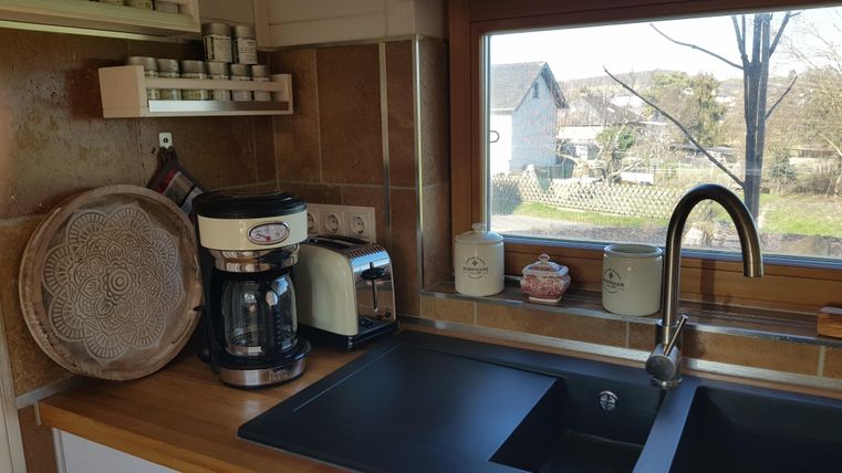 Eine moderne Küche mit einem schwarzen Waschbecken, einer Kaffeemaschine und einem Wasserkocher. Der Blick aus dem Fenster zeigt eine ruhige Landschaft mit Bäumen und Häusern.