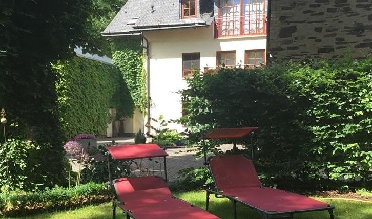 Zwei rote Liegen stehen in einem grünen Garten. Im Hintergrund ist ein charmantes Haus mit großen Fenstern zu sehen.