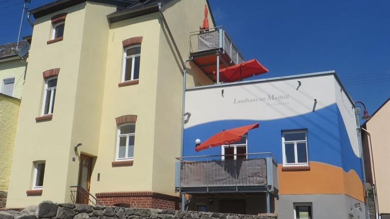 Une maison colorée avec un design mural orange et bleu. Sur le balcon, il y a des parasols rouges.