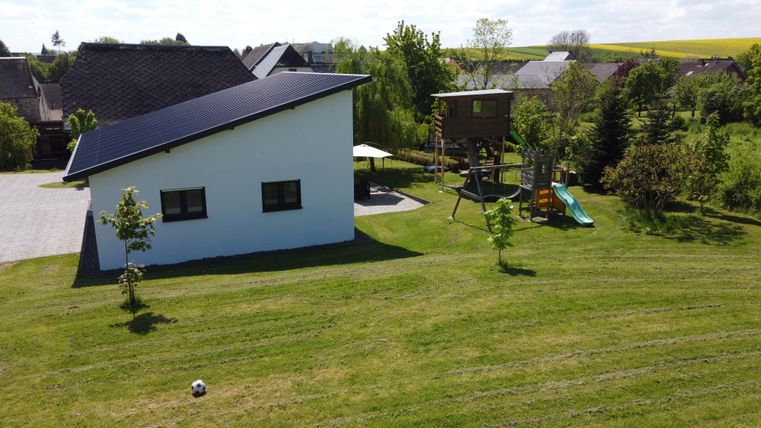Une maison moderne avec un jardin soigné. En arrière-plan, on peut voir une aire de jeux et un coin salon.