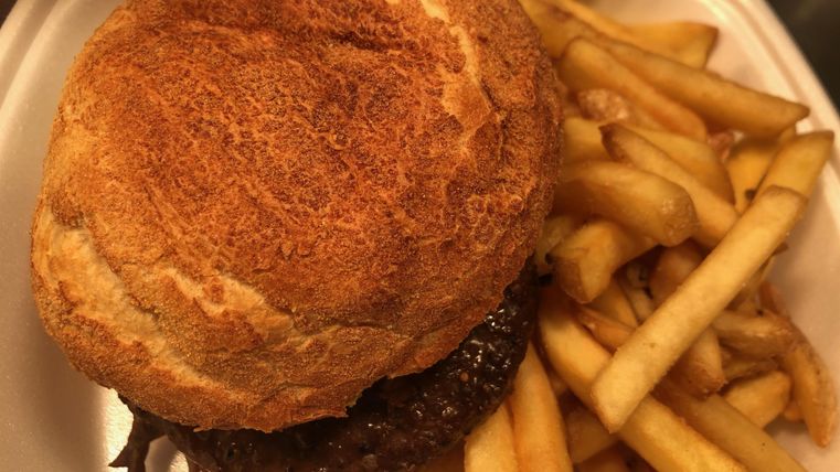 Ein saftiger Burger mit einer knusprigen Brötchen und einer Portion Pommes frites. Das Gericht ist appetitlich angerichtet und ideal für einen schnellen Snack.
