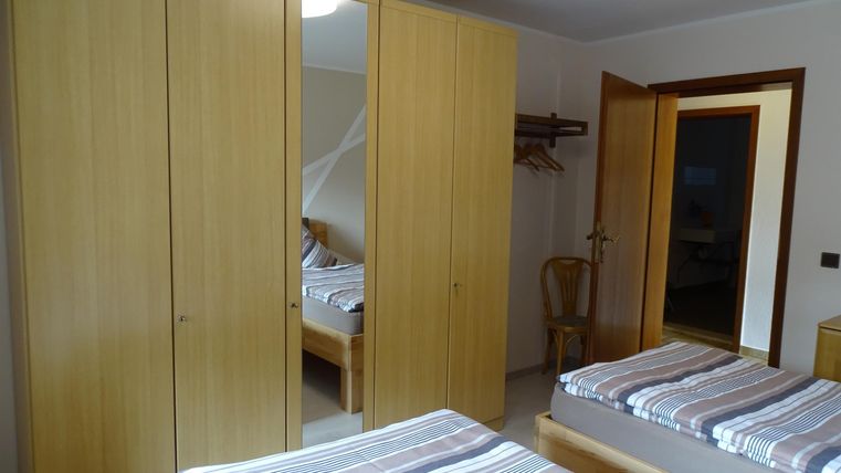 Een eenvoudige slaapkamer met twee bedden en een grote kast. De muren zijn licht en de ruimte lijkt vriendelijk en uitnodigend.