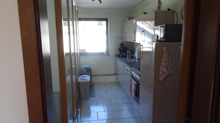 Eine moderne Küche mit hellen Fliesen und großen Fenstern. Die Ausstattung umfasst einen Kühlschrank und Kochgeräte.