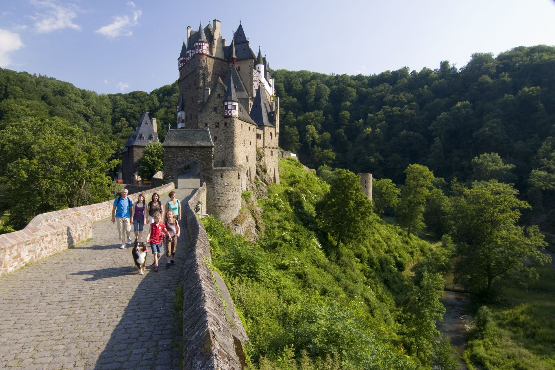 Eine Familie mit Kindern läuft vor Burg Eltz in Richtung Kamera